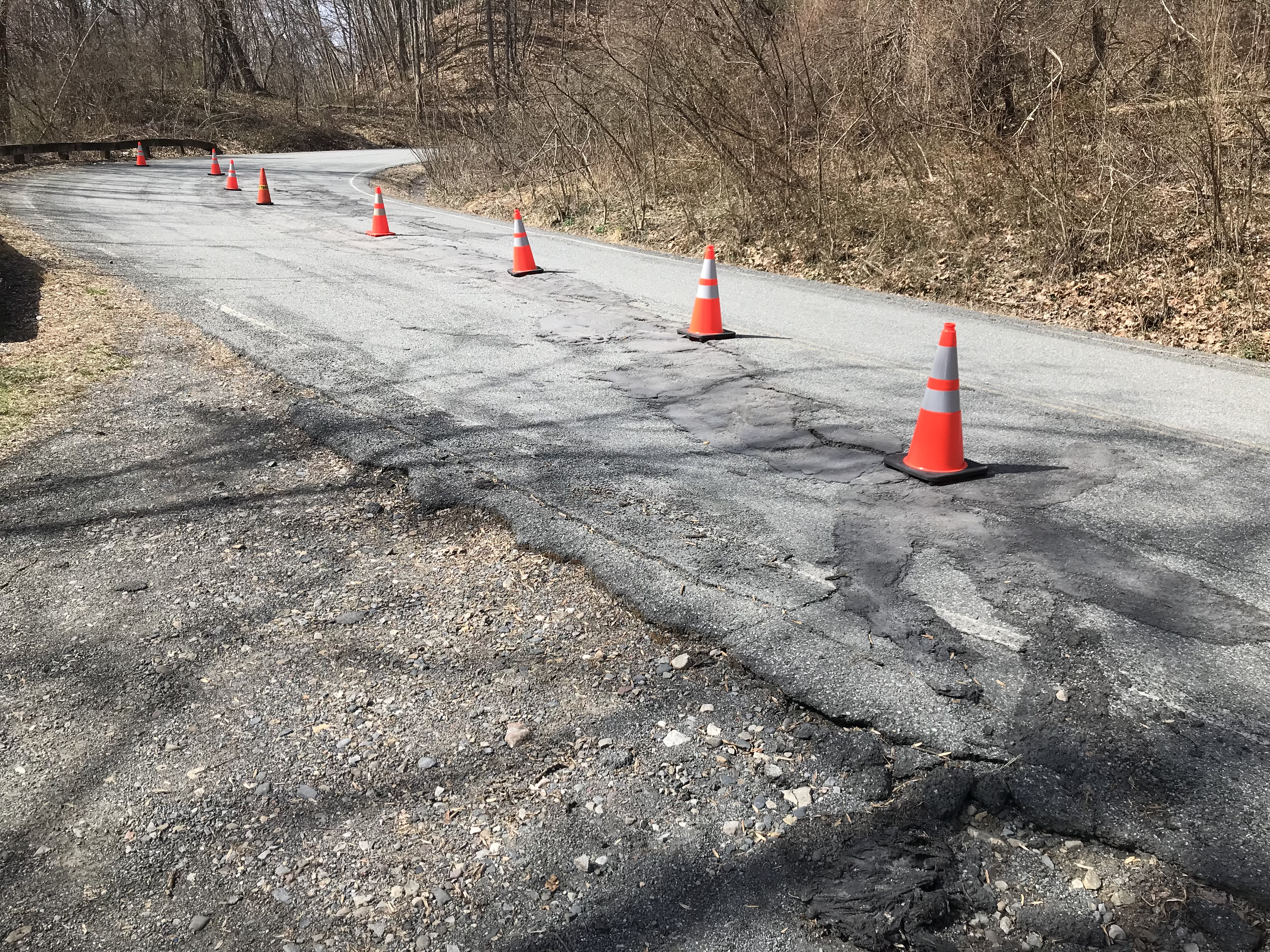 Bend in a road, with a crack that has been patched. Traffic cones warn that the road is becoming uneven.