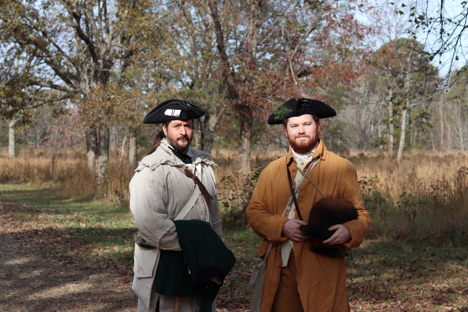 Two men in living history clothing stand in a field.