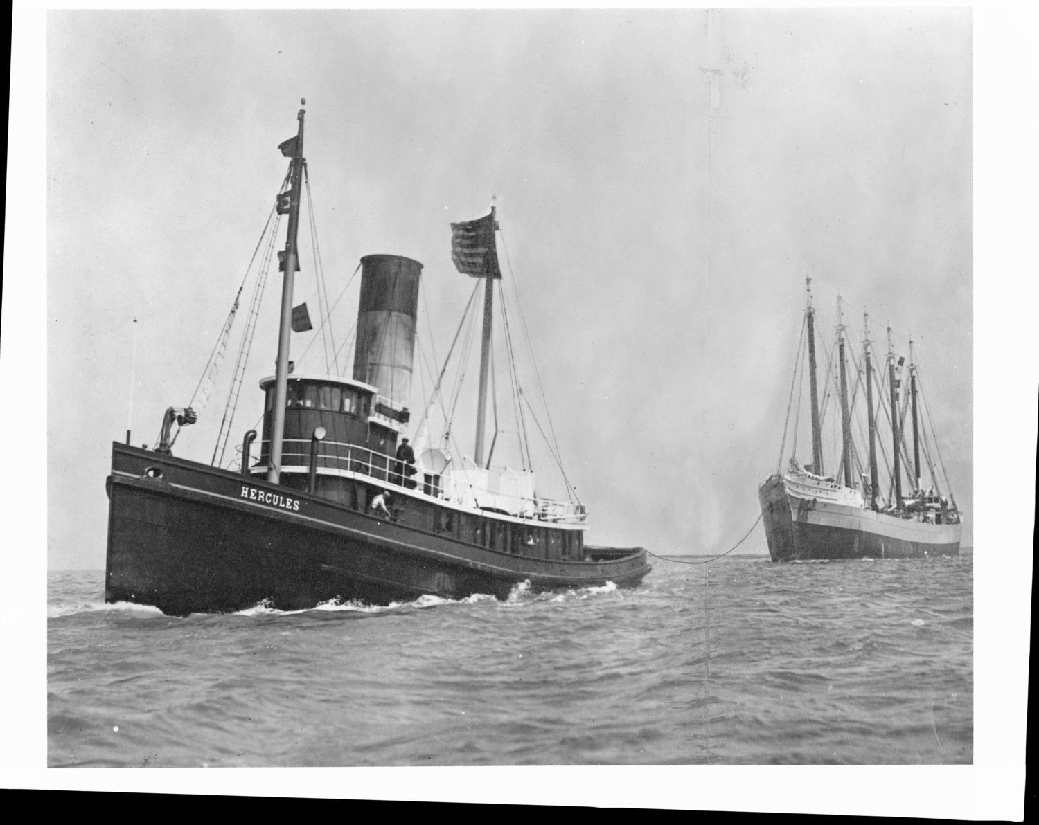Black and white photo of steamship towing a sailing ship.