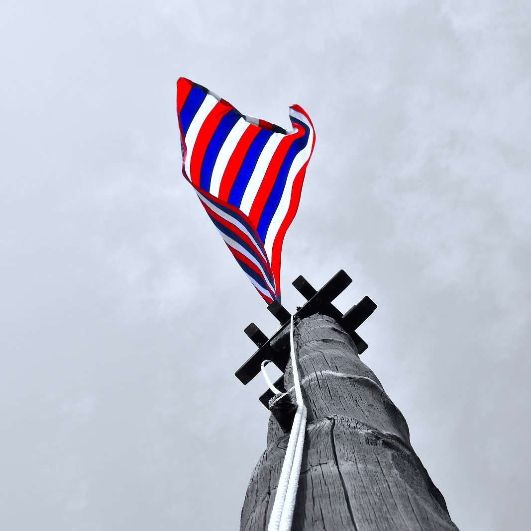A red, white and blue flag flies from a wooden flag pole on a clear day.