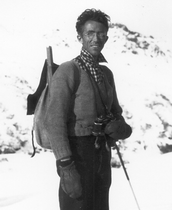 Adolph Murie stands in a snowy valley holding his binoculars 