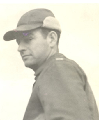 Pilot dressed in flight suit looks back at camera. He is wearing a baseball cap.