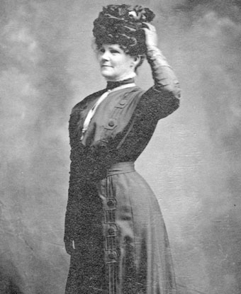 Woman standing with hand on her hat.
