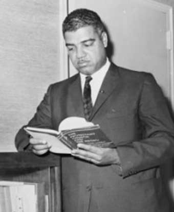 Whintey in suit, leaning against bookcase, reading a book