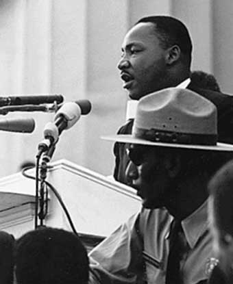B&W photo of MLK at podium with park ranger seated below