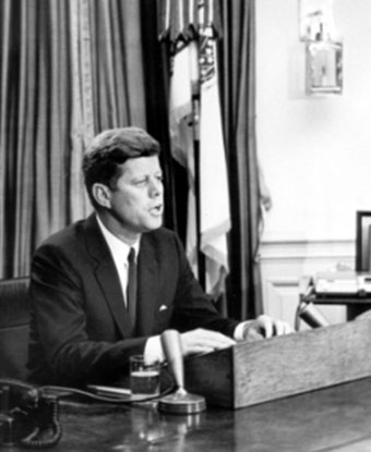 B&W photo of JFK seated at desk with microphone addressing nation