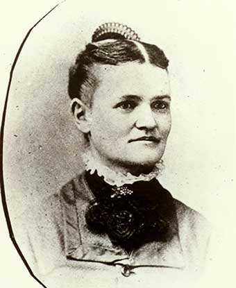 A 1879 portrait photo depicts a woman in a dress with parted hair and a comb. A 1879 portrait photo depicts a woman in a dress with parted hair and a comb.