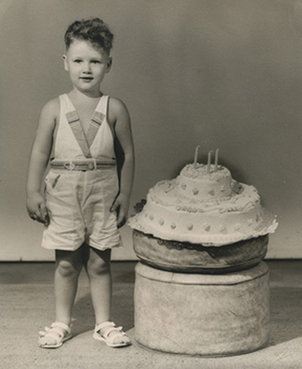 Billy Blythe III (youg Bill Clinton) standing next to a cake on his thrid birthday.