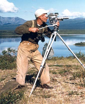 Dick Proenneke looking through the viewfinder of a camera on a tripod