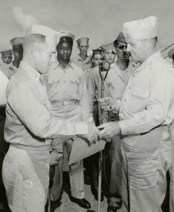 Black and White photograph of officers in Navy uniform. Crewmembers watch in background.