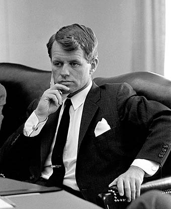 Robert F. Kennedy seated on leather sofa with right hand to chin. 