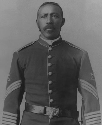 A soldier wearing a dark colored uniform standing at attention