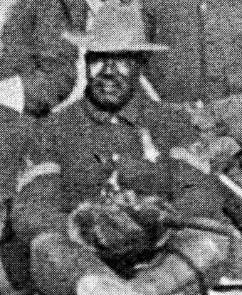 A soldier sits for a portrait wearing a dark colored uniform and stetson hat