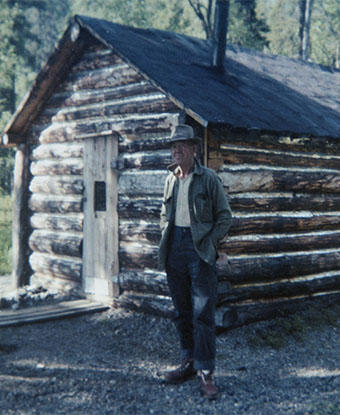 Man wearing hat in front of log cabin