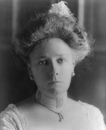 A lady with large hair wearing a tiara and a white gown and elbow-length white gloves