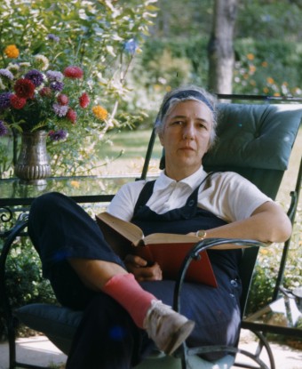 A woman seated in a chair outoors with a book in her hands.