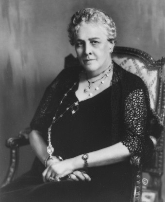 A dignified woman seated and wearing a formal black gown.
