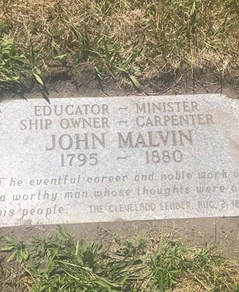 A gray, engraved rectangular headstone surrounded by dirt and grass reads: "John Malvin, 1795-1880".