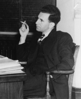 A young man in suit seated at a desk.