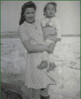 A woman holding a young child stands and smiles at the camera.