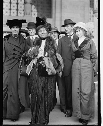 A group of three women standing with several men behind them.