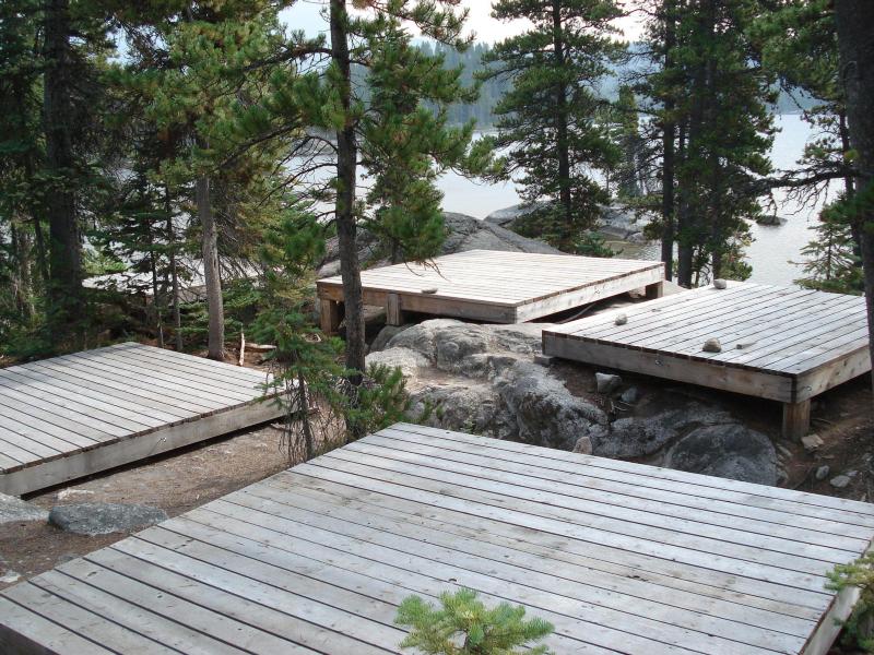 Wooden tent platforms among trees in front of a lake