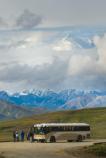 people outside of a bus, looking at a huge mountain in the distance