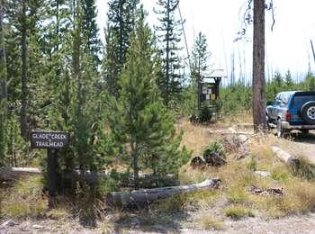 Glade Creek trailhead access showing small trail sign, information sign, parked vehicle in an area burned during the 1988 fires.