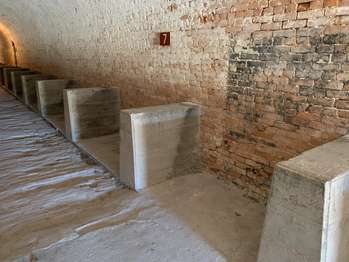 White interior brick fort walls with several small stone shelves built from the ground into the side of the wall . A brown metal sign with the number,