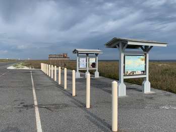 National Park Service signs under small, kiosk structures. Fort Pickens entrance sign in the background.
