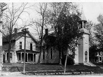 A two story frame house stands next to plain church with a round belfry.