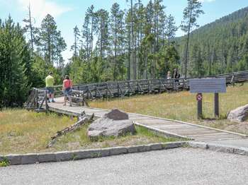 Two visitors start out down the boardwalk trail past a large wooden warning sign.