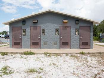 A grey stone building with four brown metal doors. Next to each door are brown metal shower and restroom signs. The second door from the left has a handicap sign.