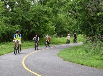 A family rides their bikes on the multi-use path as it cuts through lush greenery.