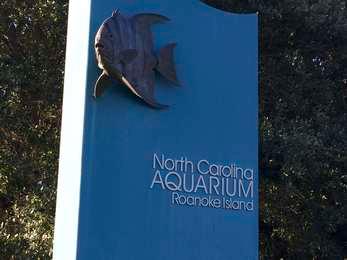 Blue entrance sign to the aquarium with a metal sculpture of a fish on the top next to the aquarium's name