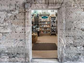 The Museum store entrance is in the Sally Port space, on the west side, across from the visitor desk. To enter the bookstore you ascend a gentle slope that is carpeted. On your left, as you enter the store, is a cashier’s counter that has small gift items. Along the walls are tall bookcases filled with a variety of books, souvenirs and other sale items. Above the shelves are various framed posters for purchase. The passport book stamping station can be found to the right of the entrance.