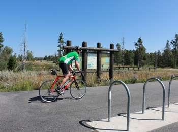 Bicyclist riding past Taggart Lake Pathway signs on multi-use pathway.
