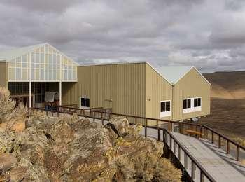 The large tan and white interpretive center building sits on the edge of a rocky bluff that overlooks dry grassland