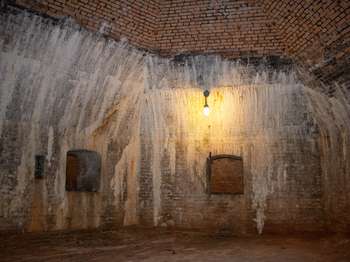 Small room with brick walls. Two of the walls have a small opening showing more of the interior of the fort.
