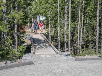 Two hikers in front of the large trailhead sign as they return from a hike.