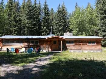 The Murie Ranch Homestead Cabin. A larger log cabin with a small front porch and cobblestone chimney. Eight brightly painted metal chairs are in a circle in front of the cabin.