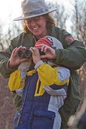 A smiling park ranger helps a young visitor with binoculars.