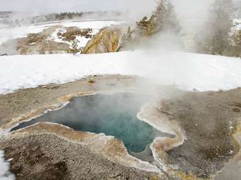A star-shaped hot spring in the middle of bare ground on a snowy winter day.