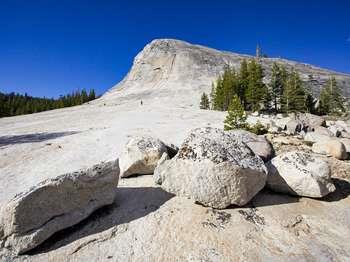 People walk on granite bedrock that curves upward into a large dome.