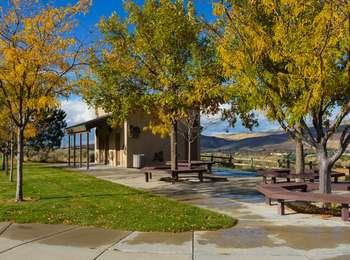 Small neighborhood park with wood benches, trees in fall color, concrete sidewalks, and a white building