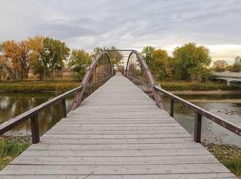 A historic wood bridge with steel supports spans the width of the shallow, muddy North Platte River