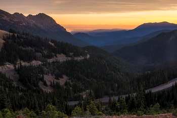 A road winds down through the mountains at sunset.