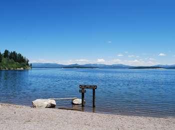 Gravel boat launch at Spalding Bay with small brown wooden sign. Jackson Lake beyond with eastern shore in the distance.