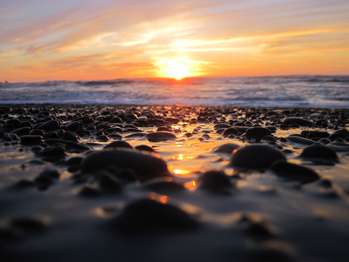 A sunset over a rocky beach with a rushing tide.