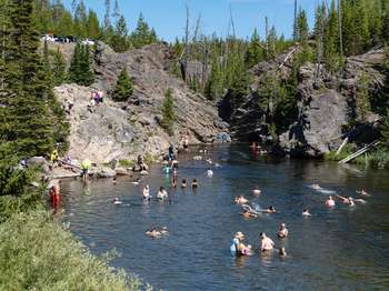 A large group of visitors playing in the water of a river flowing through a rocky canyon.